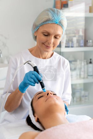 Photo for Professional female cosmetologist doing hydra-facial procedure in cosmetology clinic. Doctor using hydra vacuum cleaner. Rejuvenation and cosmetology concept - Royalty Free Image