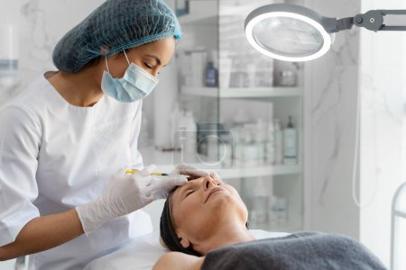 Cosmetologist looking at the senior patient while doing injections for lips augmentation and anti wrinkle procedure. Women's cosmetology in the beauty salon concept 