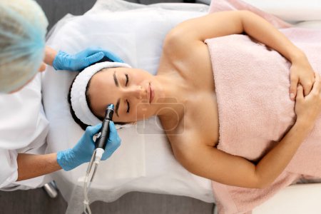 Hardware cosmetology. Closeup portrait of female face with closed eyes getting microdermabrasion procedure in a beauty parlour 