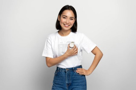 Foto de Mujer asiática positiva demostrando un desfibrilador cardioversor implantable (DAI) en las manos mientras mira a la cámara con una sonrisa agradable. Cuidado de la salud y concepto del corazón - Imagen libre de derechos