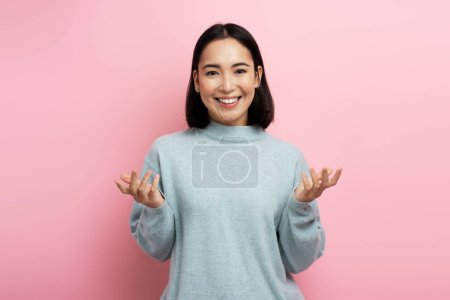 Portrait of positive confused girl in sweater expressing doubts and bewilderment, looking at camera with question. Indoor studio shot pink background 