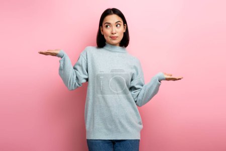 Photo for No idea, I don't know! Portrait of uncertain confused girl in sweater expressing doubts and bewilderment, looking at camera with question so what, who cares. Indoor studio shot pink background - Royalty Free Image
