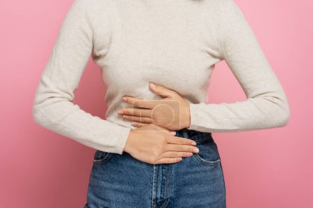 Photo for Cropped view of woman clutching belly suffering stomach ache, gastritis or constipation. Indoor studio shot isolated on pink background. Abdominal pain, periods cramps concept - Royalty Free Image