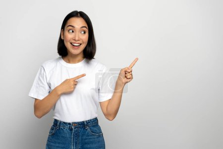 Fröhliche positive Frau, die den Finger wegzeigt und Platz für Ihre Werbung zeigt, mit einem zahmen Lächeln. Indoor-Studio isoliert auf weißem Hintergrund aufgenommen 