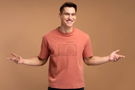 Photo for Don't know, who cares. Confused hipster guy standing with no idea gesture, shrugging shoulders raising hands. Indoor studio shot isolated on beige background - Royalty Free Image