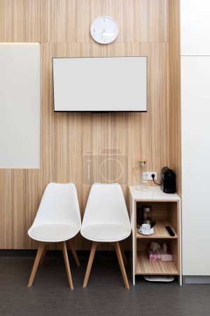 Photo for Two white chairs in the hospital room ward, an empty monitor hangs on the wall, copy space. - Royalty Free Image