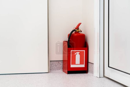 Red fire extinguisher stands in the corner of the room. Life safety concept.
