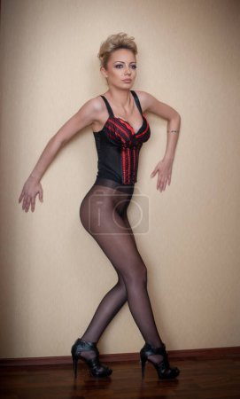 Photo for Charming young blonde woman in black corset and tights leaning against wooden wardrobe. Sexy gorgeous short hair girl near vintage wardrobe. Full length portrait of sensual female posing provocatively - Royalty Free Image