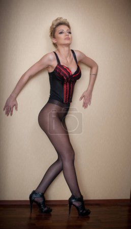 Photo for Charming young blonde woman in black corset and tights leaning against wooden wardrobe. Sexy gorgeous short hair girl near vintage wardrobe. Full length portrait of sensual female posing provocatively - Royalty Free Image