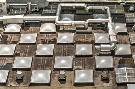 Téléchargez les photos : Piper et autres machines de climatisation sur un toit avec un motif répétitif de puits de lumière - en image libre de droit