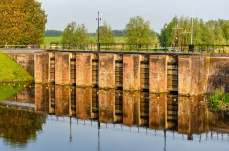 Benedensas, The Netherlands, May 10, 2024: the historic brick water outlet reflecting in motionless water during the golden hour