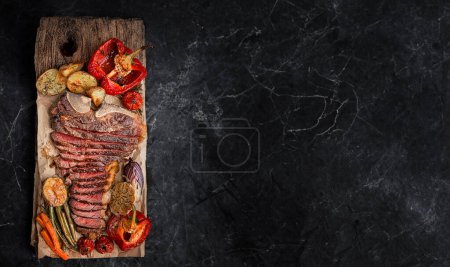 Téléchargez les photos : Steak de bœuf marbré sur l'os cuit à un état de grill moyen rare. à côté du steak, légumes grillés servant de plat d'accompagnement. charmant dîner de gala pour deux - en image libre de droit