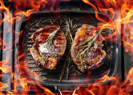 Téléchargez les photos : Cuire des steaks somptueux dans une poêle à griller avec du beurre étalé sur le steak assaisonné de poivre moulu et du sel avec des brins de romarin - en image libre de droit