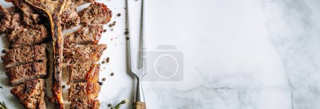 Foto de Filete de hueso t jugoso recién cocinado con romero y especias de ajo sobre un fondo de mármol claro - Imagen libre de derechos
