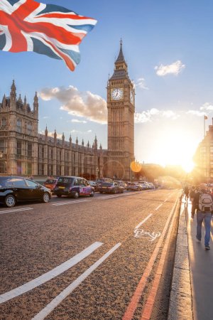 Photo for Big Ben with cars on the bridge and flag of England against colorful sunset in London, England, UK - Royalty Free Image