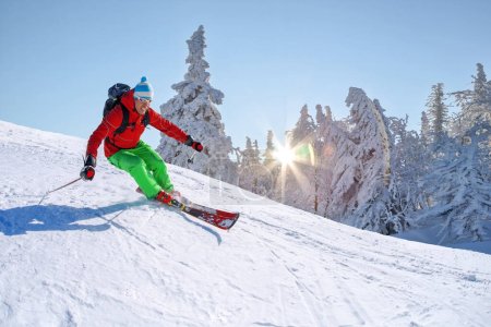 Skifahrer fährt im Hochgebirge vor blauem Himmel abwärts.