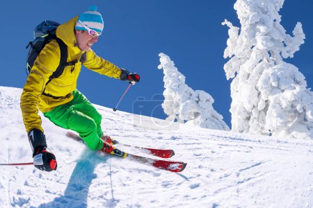 Foto de Esquiador esquiando cuesta abajo en las altas montañas contra el cielo azul
. - Imagen libre de derechos
