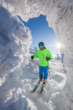 Téléchargez les photos : Skier posing in front of ice cave in high mountains against sunset. - en image libre de droit