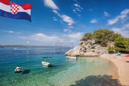 Bandera croata contra la playa de Punta Rata con barcos en Brela, Makarska, Dalmacia, Costa croata