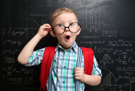 Foto de Divertido niño pequeño con gafas cerca de pizarra con diferentes fórmulas - Imagen libre de derechos