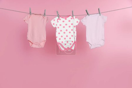 Photo for Baby onesies drying on laundry line against pink background - Royalty Free Image