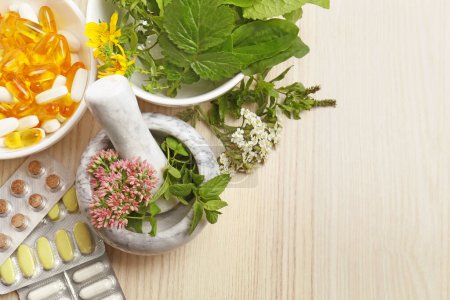 Mortar with fresh herbs and pills on wooden table, flat lay. Space for text