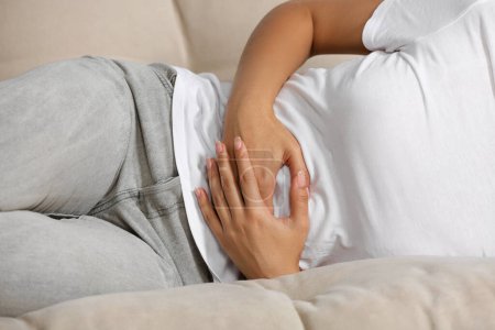 Young woman suffering from menstrual pain on sofa, closeup