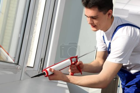 Téléchargez les photos : Worker sealing plastic window with caulk indoors. Installation process - en image libre de droit
