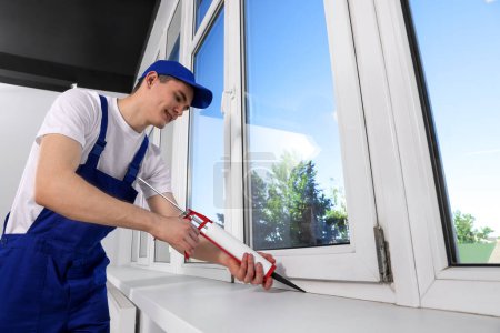 Téléchargez les photos : Worker sealing plastic window with caulk indoors. Installation process - en image libre de droit