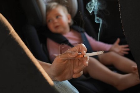 Téléchargez les photos : Mère avec cigarette et enfant en voiture, gros plan. Ne fumez pas près des enfants - en image libre de droit