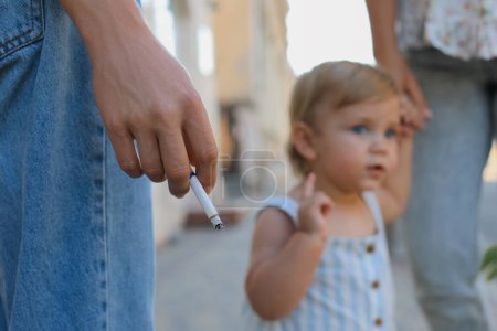 Téléchargez les photos : Femme fumant de la cigarette dans un lieu public à l'extérieur, gros plan. Ne fumez pas près des enfants - en image libre de droit
