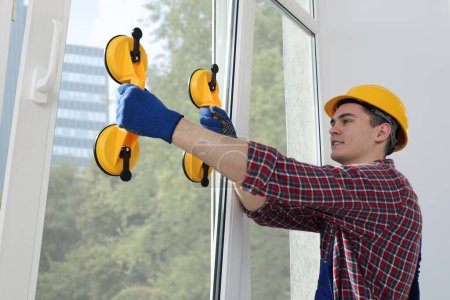 Foto de Worker using suction lifters during plastic window installation indoors - Imagen libre de derechos