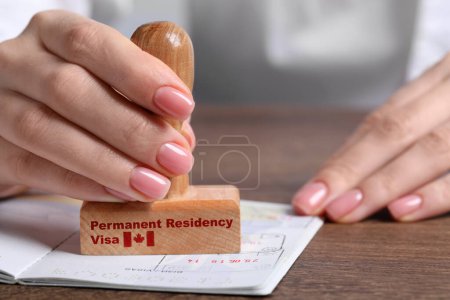 Photo for Woman stamping document at wooden table, closeup. Permanent residency visa in Canada - Royalty Free Image
