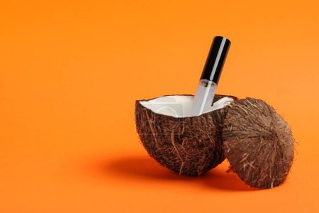 Tube Wimpernöl und frische Kokosnuss auf orangefarbenem Hintergrund. Raum für Text