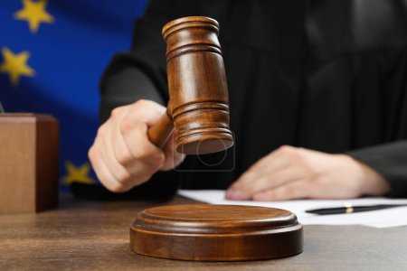 Photo for Judge with gavel at wooden table against flag of European Union, closeup - Royalty Free Image