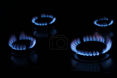 Téléchargez les photos : Gas cooktop with burning blue flames in darkness - en image libre de droit