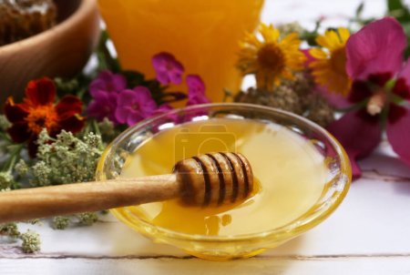 Téléchargez les photos : Miel avec trempette dans un bol et différentes fleurs sur une table en bois blanc - en image libre de droit
