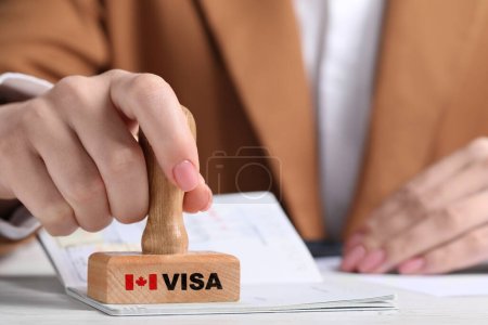 Woman stamping document at white wooden table, closeup. Visa for Canada