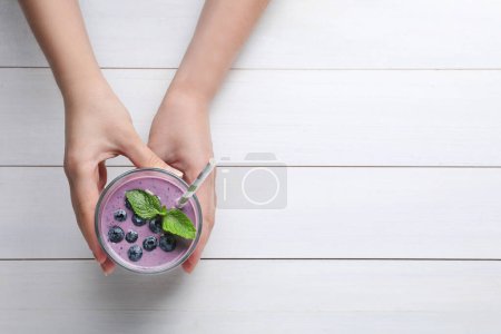 Photo for Woman with tasty blueberry smoothie at white wooden table, top view. Space for text - Royalty Free Image