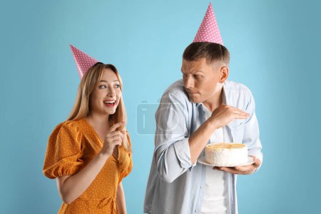 Téléchargez les photos : Homme gourmand cachant gâteau d'anniversaire de la femme sur fond turquoise - en image libre de droit