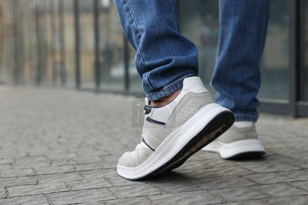 Hombre en jeans y zapatillas de deporte caminando por la calle de la ciudad, primer plano. Espacio para texto