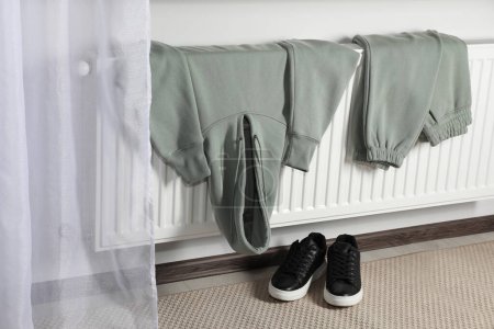 Téléchargez les photos : Chauffage radiateur avec vêtements et chaussures dans la chambre - en image libre de droit
