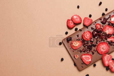 Chocolate bar with freeze dried fruits on beige background, top view. Space for text