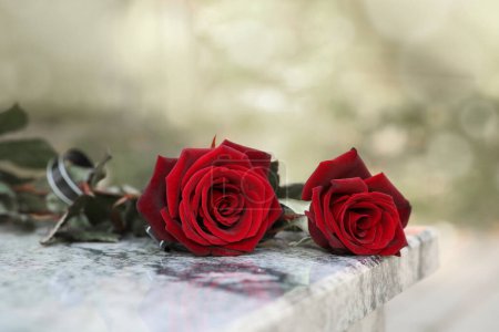 Rote Rosen auf einem Grabstein aus Granit im Freien. Trauerzeremonie