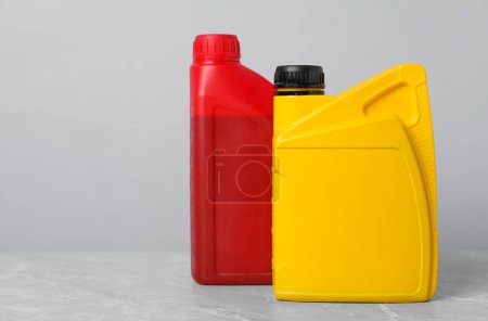 Motor oil in different canisters on grey marble table against light background, space for text