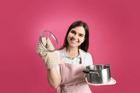 Foto de Mujer joven feliz con olla de cocina sobre fondo rosa - Imagen libre de derechos