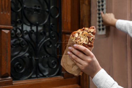 Téléchargez les photos : Femme tenant un délicieux croissant et sonnant à la porte à l'extérieur, gros plan. Espace pour le texte - en image libre de droit