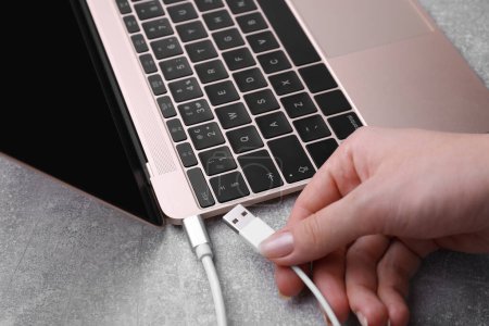 Photo for Woman holding plugged USB cable into laptop at grey table, closeup - Royalty Free Image