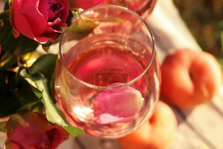 Glas köstlichen Rosenweins mit Blütenblättern und Blumen außen, Nahaufnahme