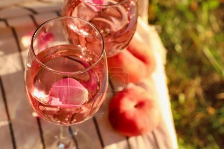 Foto de Vasos de delicioso vino de rosas con pétalos y melocotones en la manta de picnic blanco en el exterior. Espacio para texto - Imagen libre de derechos